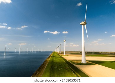 A row of elegant wind turbines stand tall next to a serene body of water, harnessing the power of the wind to generate renewable energy in the Netherlands - Powered by Shutterstock