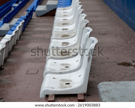 A row of empty bleachers sit on a concrete surface. The bleachers are white and appear to be dirty