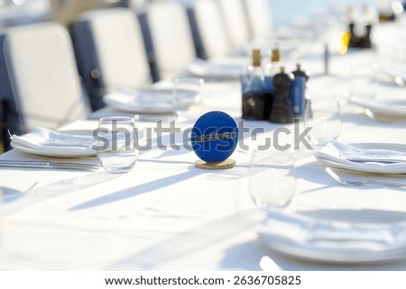 A row of empty plates on a long table with a white tablecloth. A table in a Mediterranean restaurant ready to serve a large group of visitors or tourists. A summer veranda of a restaurant by the sea
