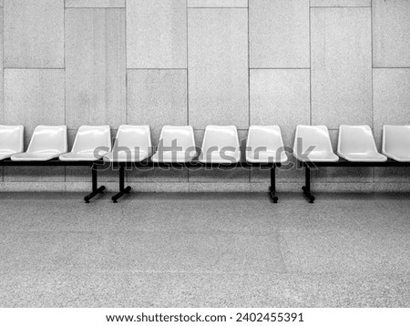 Row of empty white waiting plastic chairs seats with black iron legs seats on grey tiles and concrete wall background inside the modern building with nobody. 