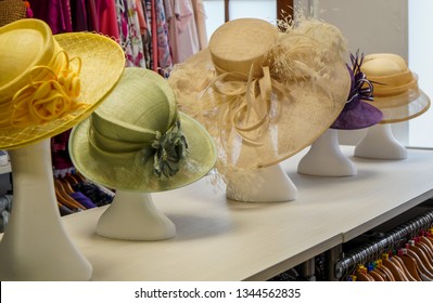 A Row Of Fancy Ladies Hats As Worn On Race Day Or At Weddings By The Bride's Mother. Pastel Yellow, Pale Green And Beige With Fancy Frills, Ribbons And Feathers. Displayed On Polystyrene Heads.