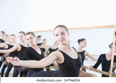 Row Of Female Ballet Dancers Practicing At Barre In Rehearsal Room