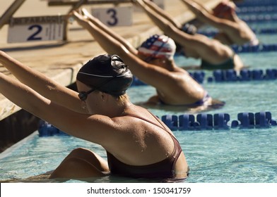 Row of female swimmers holding onto starting block preparing to swim backstroke