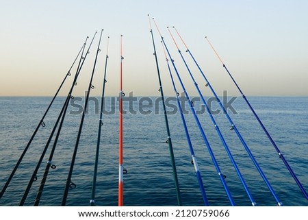 A row of fishing rods lined up to the sea. Beautiful sea sunset background with fishing poles. Man's holidays concept photo. Landscape at sunset.