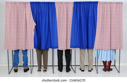 A row of five voting booths with men and women casting their ballots at a polling place. Horizontal format, only showing the legs of the voters, people are unrecognizable..