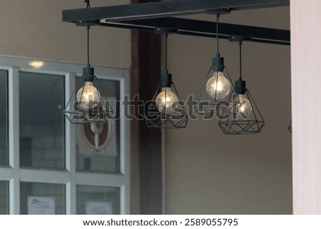 A row of four lights hanging from a ceiling. The lights are on and are lit up. The lights are hanging from a metal frame
