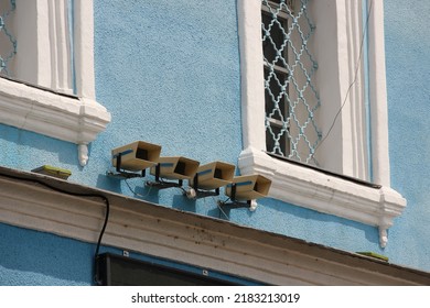 Row of four loudspeakers for notification on blue plastered wall of historical aincient building, windows with lattices
