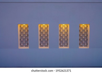 Row of four similar decorative exterior windowlike features with patterned insets, each illuminated, on a concrete building at twilight in a beach town along the Gulf Coast of the Florida Panhandle