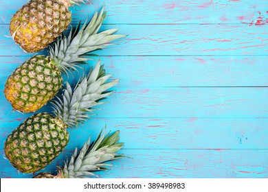 Row Of Four Slanted Pineapple Fruits Laid Down On Old Blue Wooden Floor Or Table With Copy Space