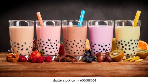 Row of fresh boba bubble tea glasses on wooden background. Slices of fruity ingredients with delicious glasses of a summer refreshment.