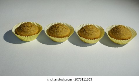 Row Of Fresh Corn Muffins In Yellow Cupcake Liners On White Background, Stylized Food Art Inspired By Painter Wayne Thiebaud. 