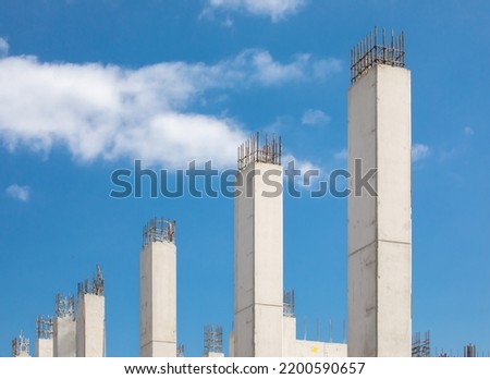 A row of freshly poured concrete pillars in a high rise construction project showing rebar reinforcing steel at the top