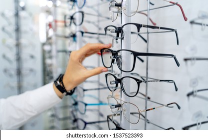 Row of glasses at an opticians. Eyeglasses shop. Stand with glasses in the store of optics. Woman's hand chooses spectacles. Eyesight correction.