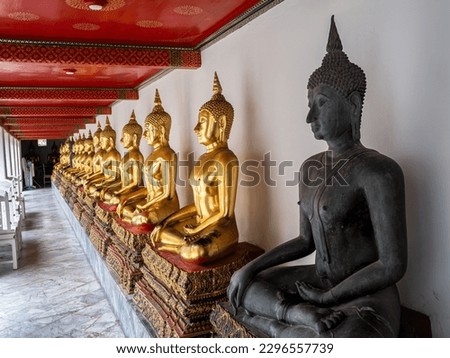 A row of gleaming golden Buddha statues lining a wall at Wat Pho Temple in Bangkok. Amidst the radiant statues, a unique black Buddha statue stands out, commanding attention.