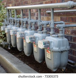 Row of gray gas meters at an apartment complex with complicated manifold piping