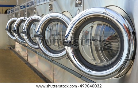 Row of industrial laundry machines in laundromat.