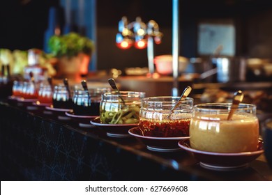 Row of jars with different sauces and condiments on counter in restaurant.