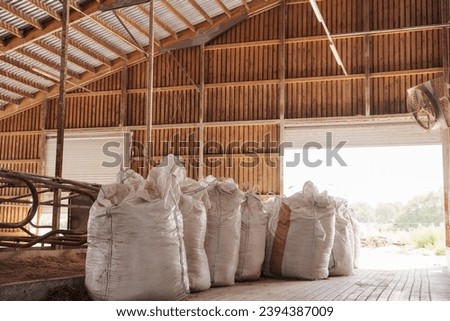 A row of large, filled industrial feed bags neatly aligned inside a rustic farm storage barn