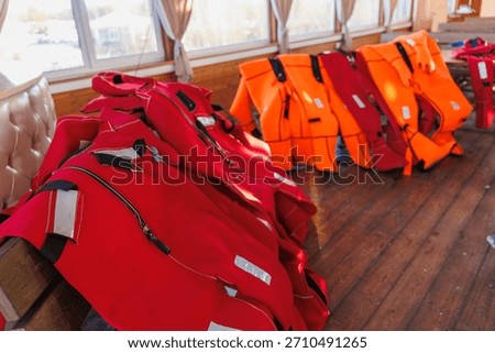 Row Of Life Jackets On Deck, Bright Red And Orange Vests Neatly Lined Along Wooden Planks Of Research Vessel,