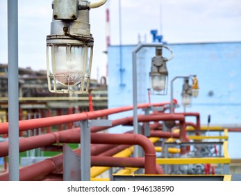 Row of lighting masts with retro design lanterns in explosion proof and fireproof design close-up over background of pipelines buildings and equipment of chemical plant with copyspace.