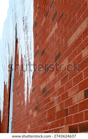 A row of long icicles hanging parallel to a red brick exterior wall on a cold winter day.
