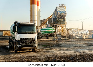 Row Many Modern Big Mixer Trucks Parked Against Mobile Temporary Concrete Plant Factory At New Asphalt Road Construction Site Early Morning Day. Heavy Machniery And Industrial Facilities Background