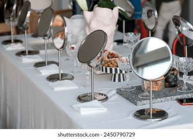 A row of metal table mirrors are lined up on a white tablecloth next to a marble tray, champagne glasses, white and black striped dish with almond nuts, paper towel sheets, a mobile phone, a pink vase - Powered by Shutterstock