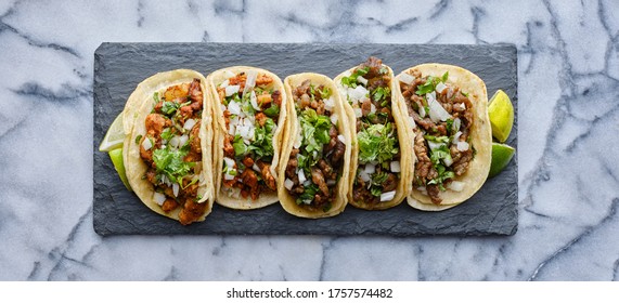 row of mexican street tacos on slate with carne asada and al pastor in corn tortilla