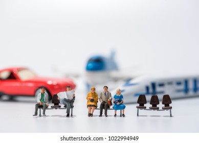 Row Of Miniature People Figure Sitting On Bench With Air Plane,car,hispeed Train Model Figure Background