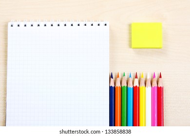 A row of multicolored pencils with a open empty notepad and a yellow eraser