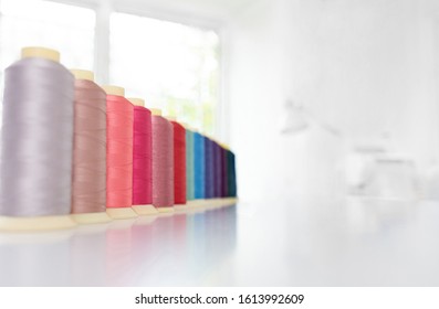 Row Of Multicolored Spools Of Sewing Threads On A White Table. Workplace Of Seamstress. Sewing Background With Copy Space.