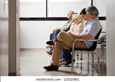 Row of multiethnic people sitting side by side while waiting for doctor in hospital lobby