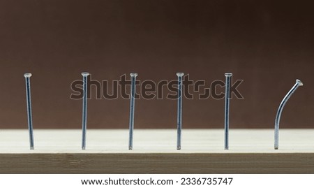 Row of nails hammered into wood and the last one bent