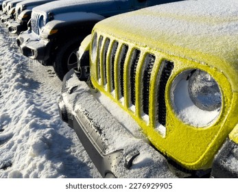A row of new 2023 Jeep 4x4 sporty Wrangler SUVs and Gladiator trucks in a line. Some are bright yellow, blue, black, and green. The recreation vehicles are covered in thick winter ice and frost snow.