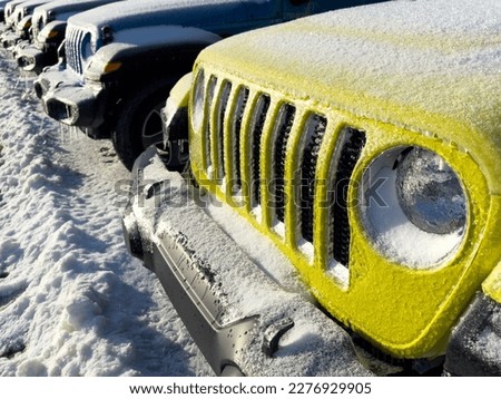 A row of new 2023 Jeep 4x4 sporty Wrangler SUVs and Gladiator trucks in a line. Some are bright yellow, blue, black, and green. The recreation vehicles are covered in thick winter ice and frost snow.