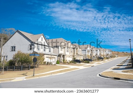 Row of new development two story houses with front garage driveway, well-trimmed landscape and large residential street suburbs of Atlanta, Georgia, USA, sunny blue cloud sky. Subdivision HOA area