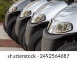 A row of new grey E Z Go Valor modeled golf carts for sale on a dealership parking lot. The small sporty electric golf cars have LED headlights,  all terrain tires, and black plastic bumpers. 