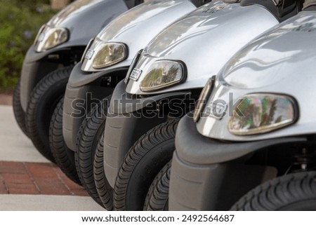 A row of new grey E Z Go Valor modeled golf carts for sale on a dealership parking lot. The small sporty electric golf cars have LED headlights,  all terrain tires, and black plastic bumpers. 