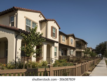 A row of new homes with fenced yards along a sidewalk.
