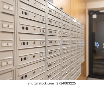A row of numbered metal mailboxes inside an apartment building lobby. The clean, organized mail slots create a modern residential setting, highlighting postal delivery, housing infrastructure, and everyday urban life.