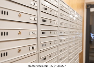 A row of numbered metal mailboxes inside an apartment building lobby. The clean, organized mail slots create a modern residential setting, highlighting postal delivery, housing infrastructure, and everyday urban life.