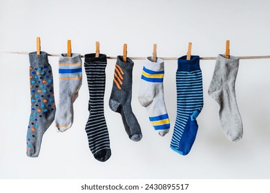 Row of odd socks hanging on clothesline against white background.