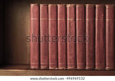 A row of old, battered, matching encyclopaedias (circa 1950s) lined up on a shelf, with titles removed to leave blank spines.  Red leather effect with gold striped trims.  Vintage effects applied.