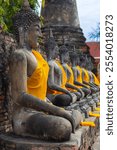 Row of old seated Buddha statues in golden robe at Wat Yai Chai Mongkol in Ayutthaya, Thailand