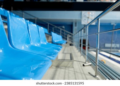 Row of plastic blue seats of empty tribune at large stadium where variety of sports matches, games, trainings and competitions take place