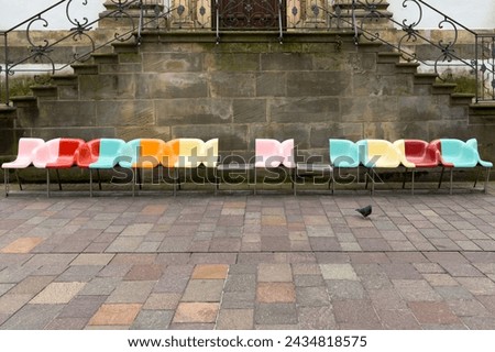 A row of plastic colorful chairs adds a pop of brightness against the backdrop of a weathered brick floor. 
