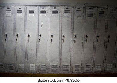 A row of poorly painted white lockers with shadows covering the sides of them. The lockers look old and worn down.