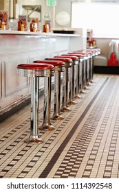 A row of red bar stools at the lunch counter in a fifties style diner.