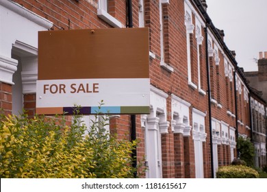 A row of red brick terraced houses with a 'for sale' sign in London