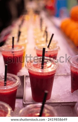row of red fruit juice on ice at a market stall
